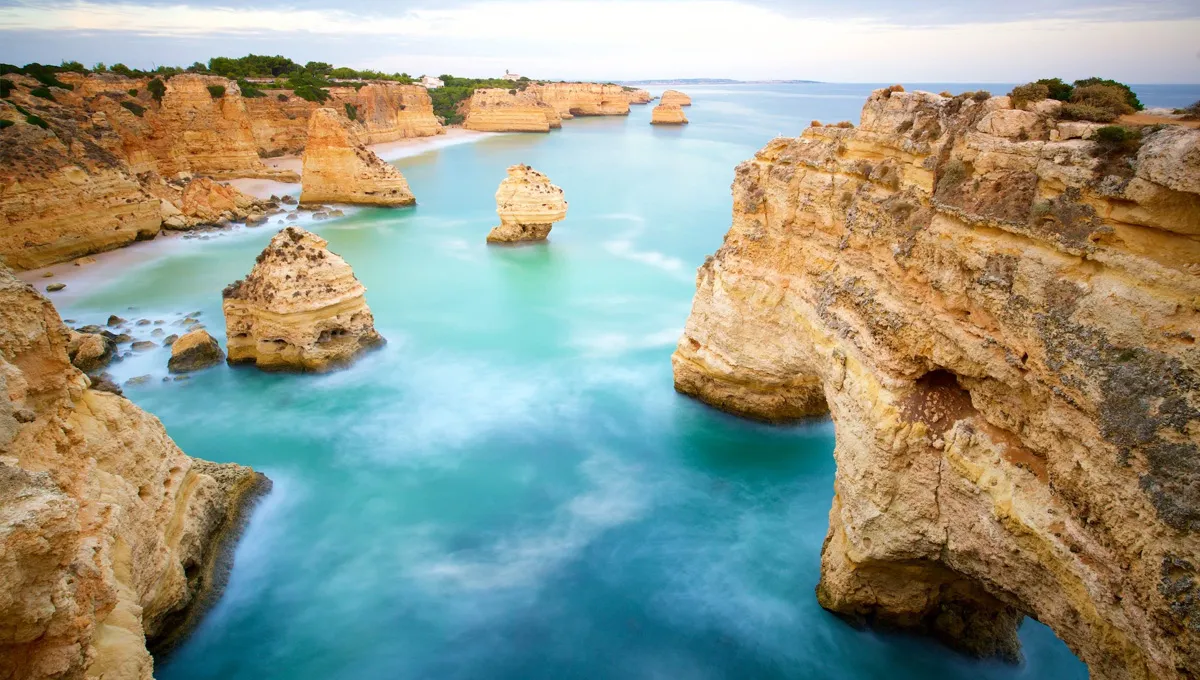 Lagos coastline in Algarve showing limestone cliffs and turquoise waters under a partly cloudy sky.