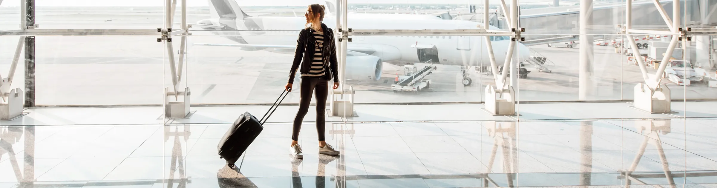 Donna con valigia in aeroporto che guarda gli aerei sulla pista pronta per il noleggio auto.