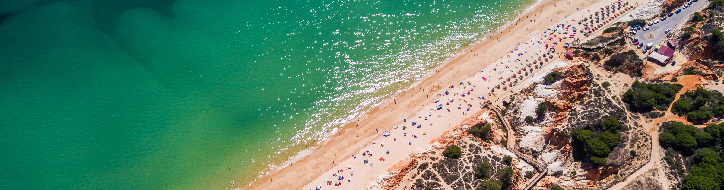 Faro strand med klar turkos vatten, sandstrand och färgglada parasoller för sommar biluthyrning.