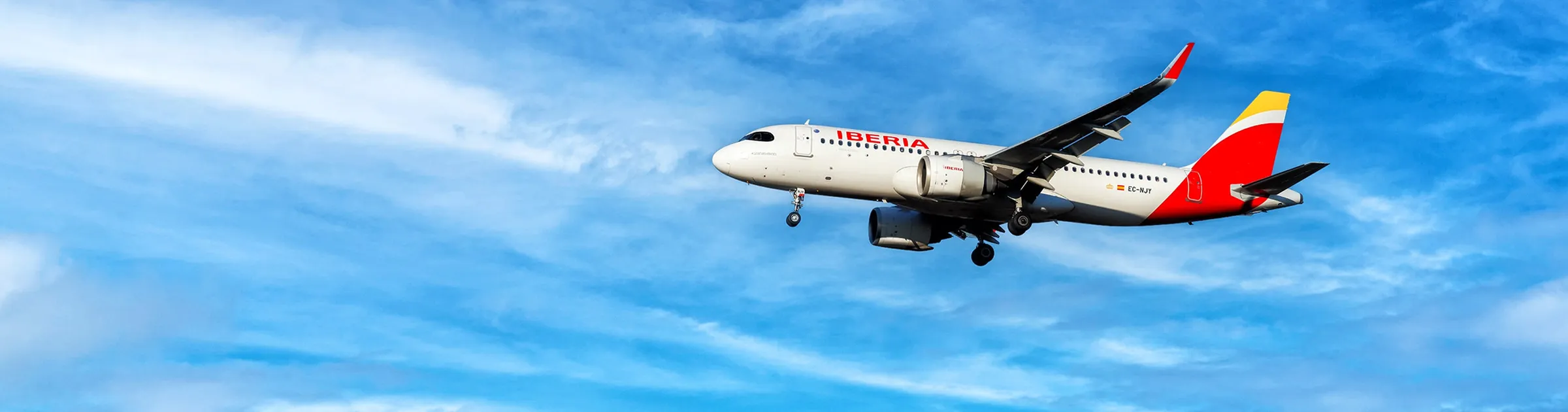 Aereo passeggeri in livrea Iberia che vola in cielo azzurro con qualche nuvola.