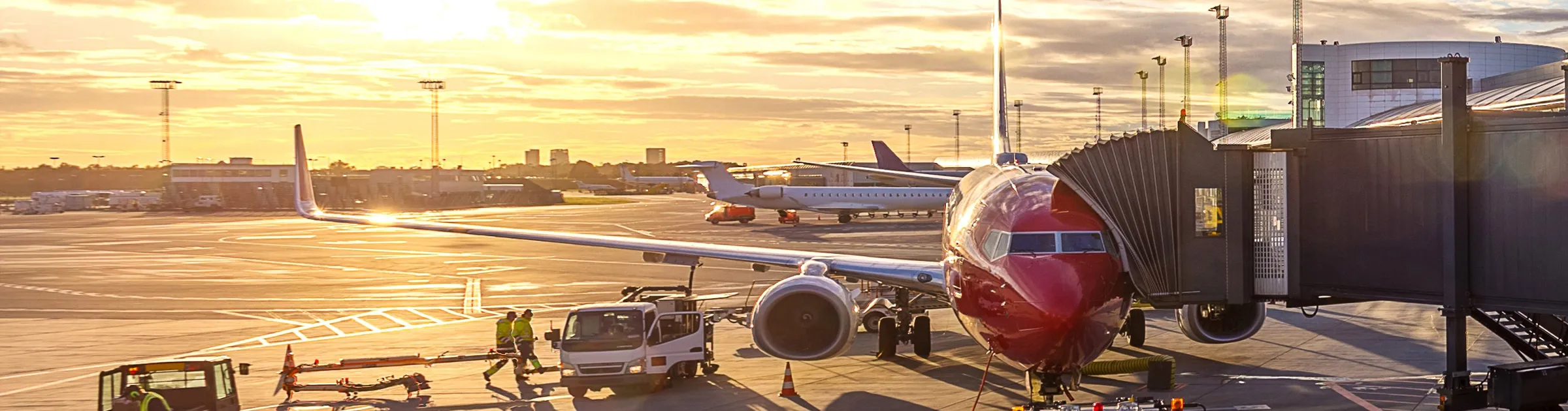 Aereo parcheggiato al gate di un aeroporto al tramonto con personale di terra e veicoli vicini.
