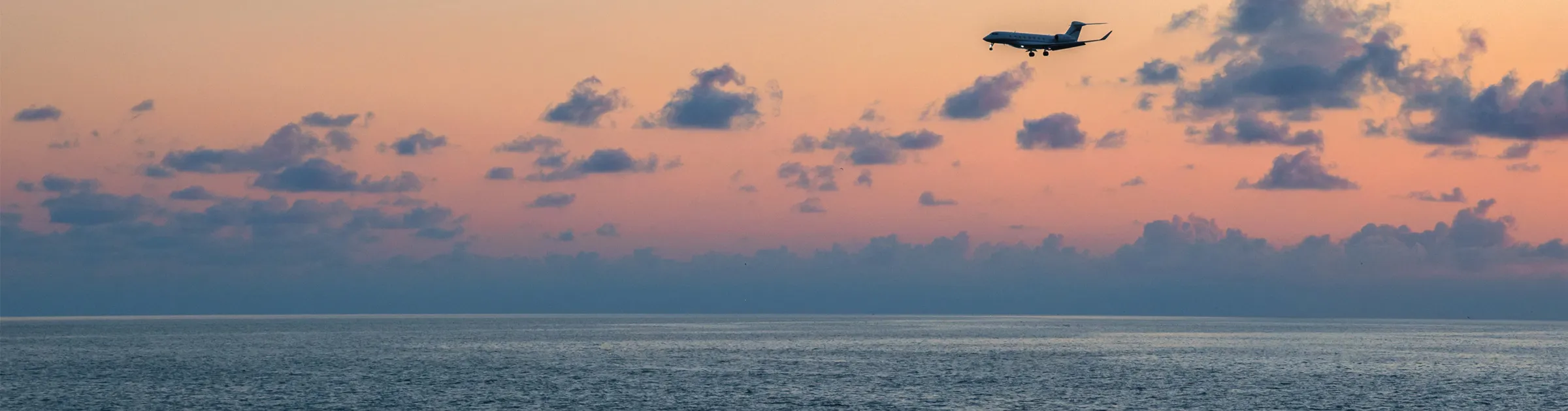 Jet privato che vola sopra l'oceano al tramonto con nuvole sparse per viaggiatori con noleggio auto.