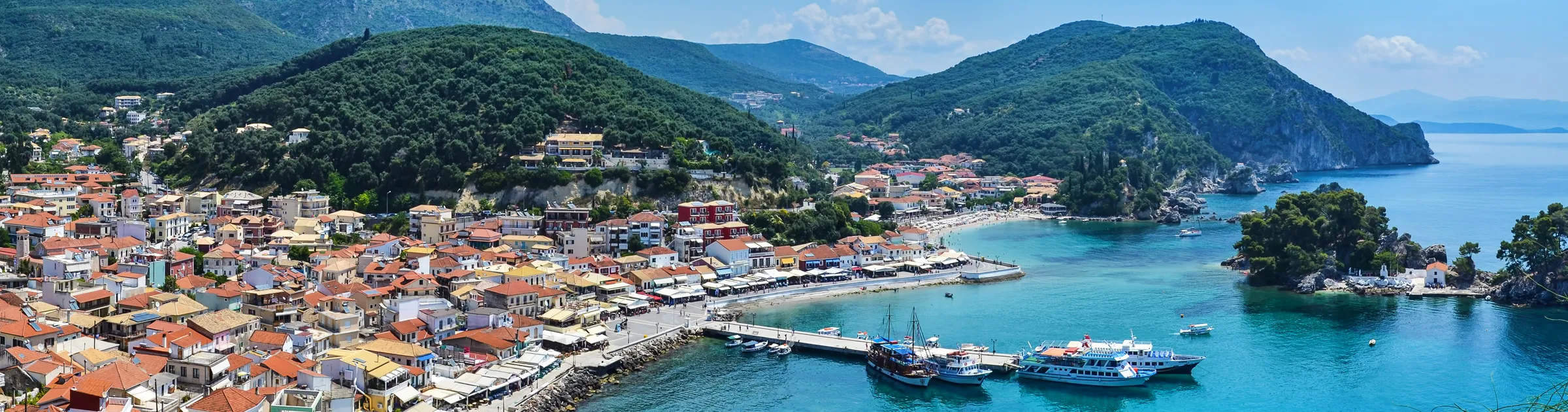Porto di Parga con vivace città costiera e colline verdi intorno al mare blu per noleggio auto.