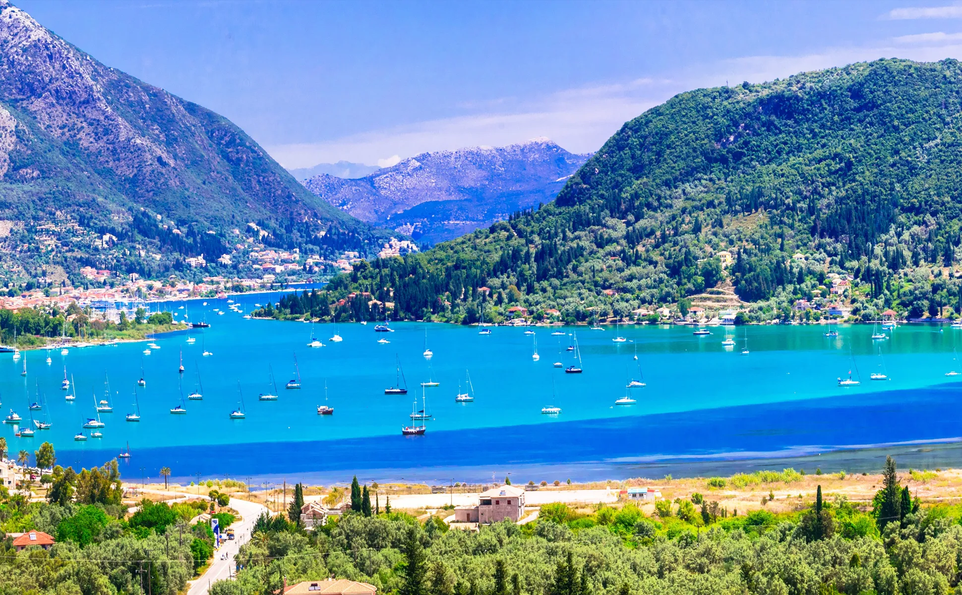 Corfu bay with boats anchored on turquoise water surrounded by green hills and mountains.