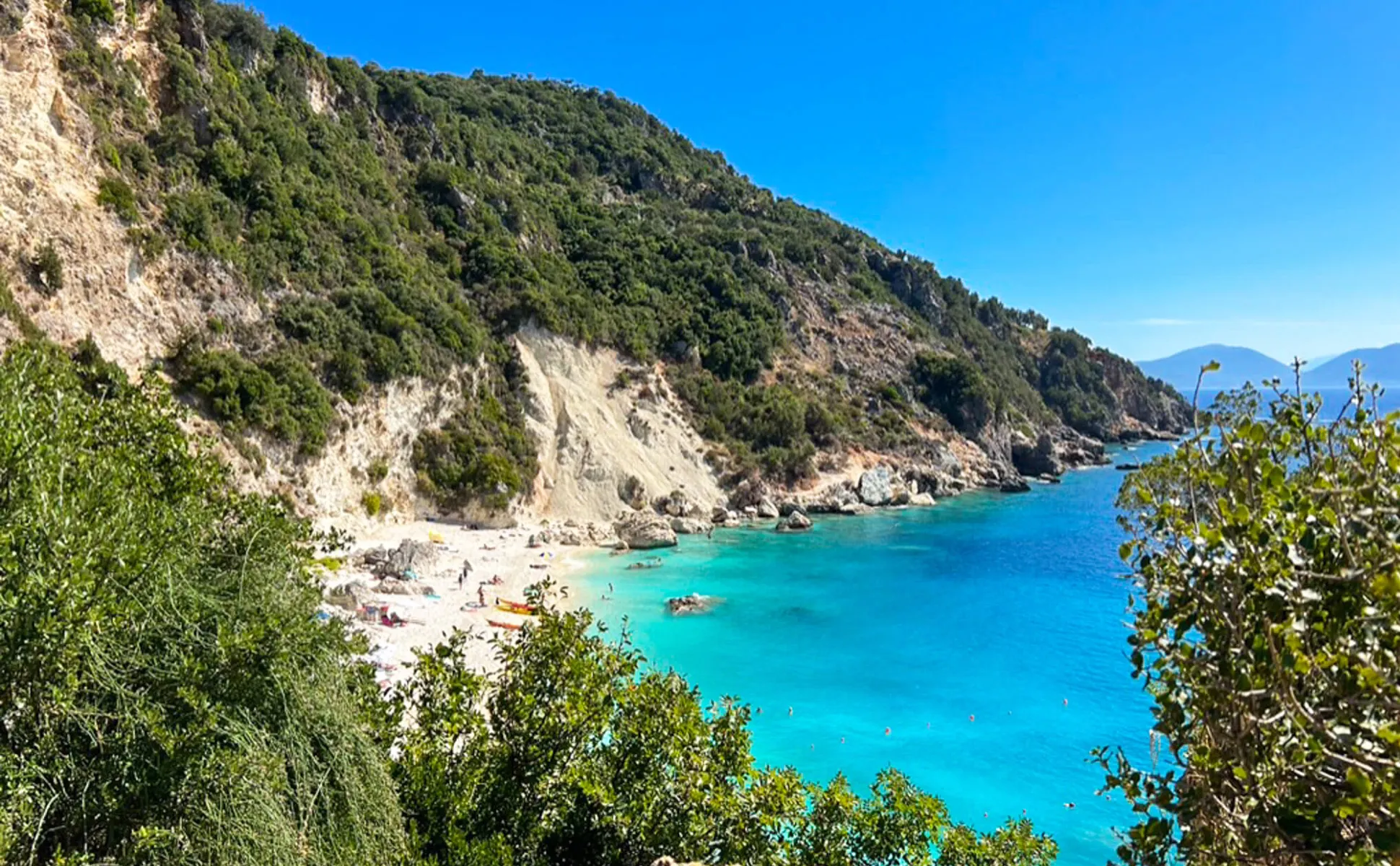 Myrtos Beach in Kefalonia with turquoise waters and a green mountainous coastline on a clear sunny day.