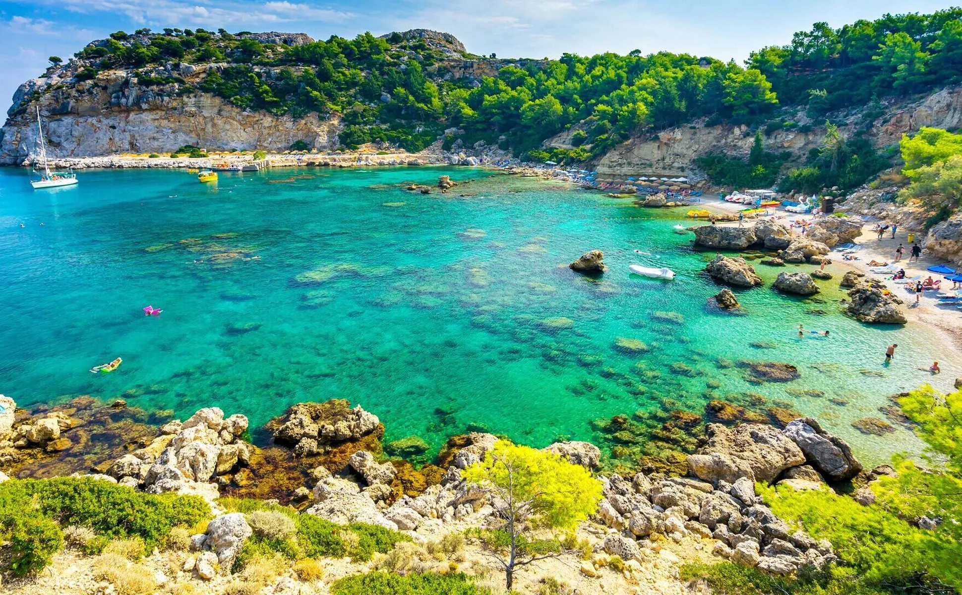 Bella baia con acqua turchese limpida, scogliere rocciose e persone che godono della spiaggia soleggiata.