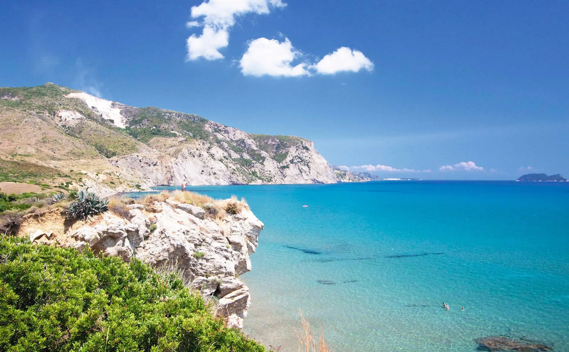 Coastal cliffs and clear turquoise sea under a blue sky with a few clouds, ideal for exploring by rental car.