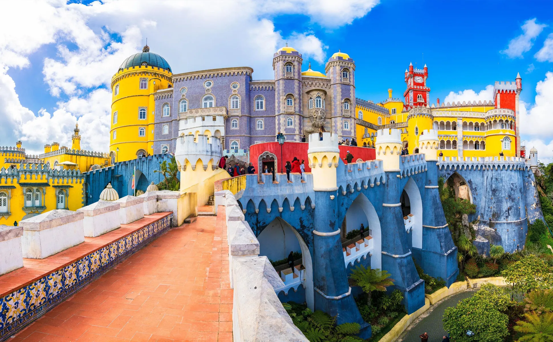 Pena Palace in Sintra, Portugal, with vibrant yellow, red, and blue walls under a partly cloudy sky.