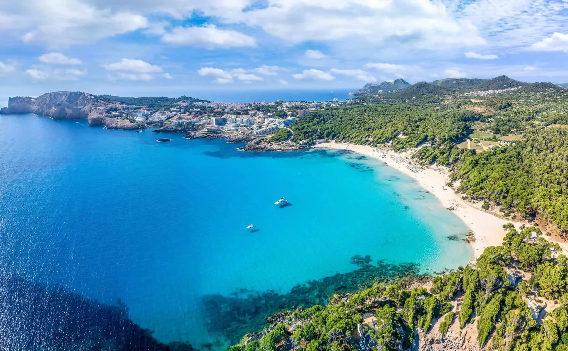 Coastal view of Cala Agulla beach in Mallorca with clear turquoise water and surrounding green hills.