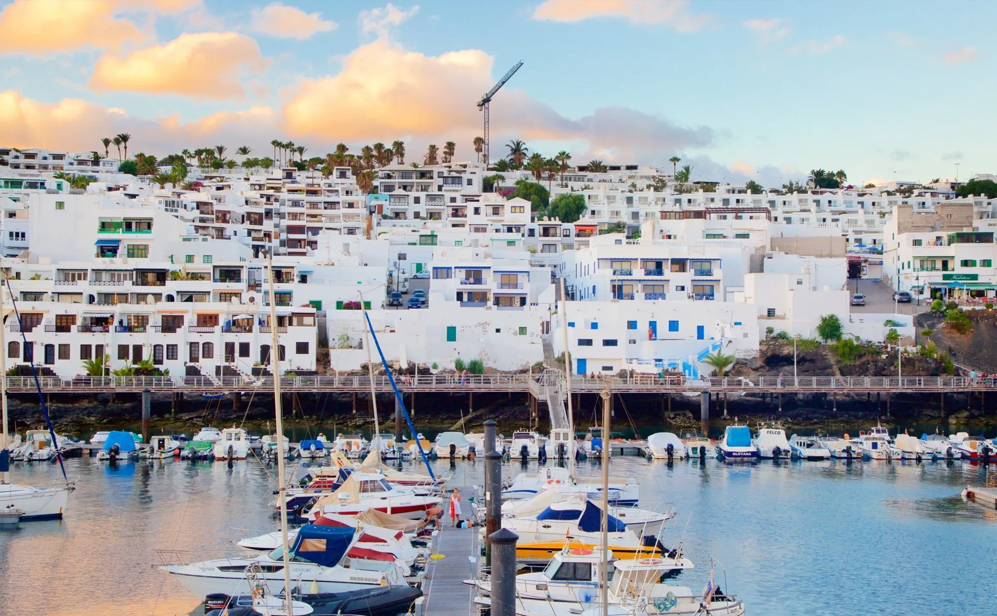 Lanzarote harbor with white buildings and boats at a marina during sunset.