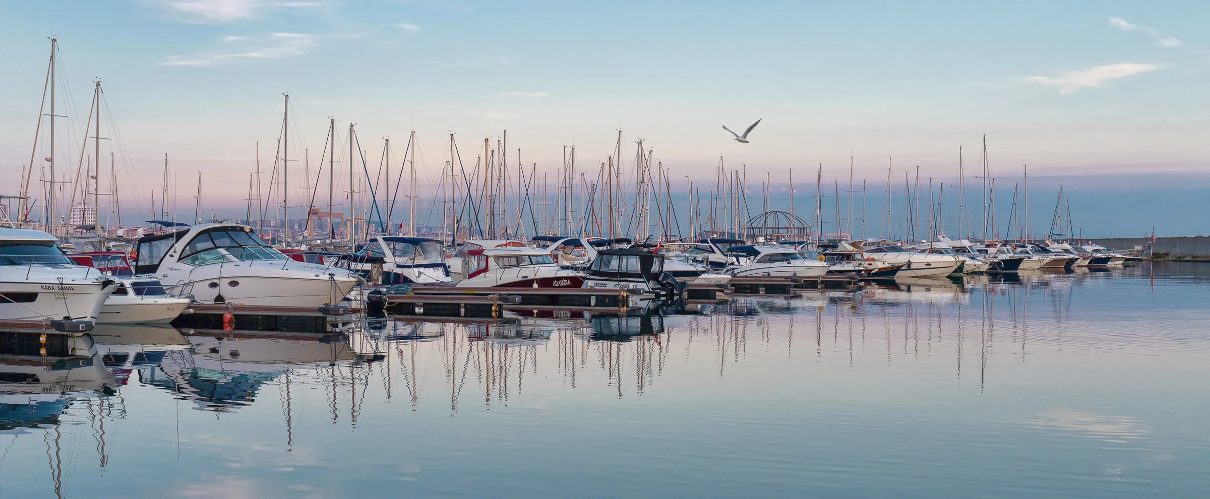 Gün batımında mavi gökyüzü altında suda dingin şekilde demirlemiş birçok tekneyle marina.