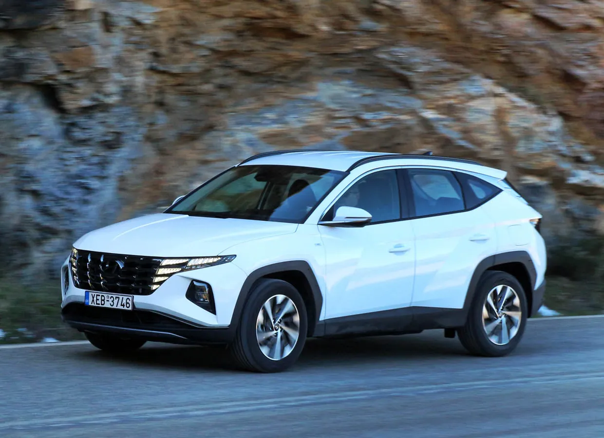 Weißer Hyundai Tucson Mietwagen fährt auf einer Bergstraße mit felsigen Klippen im Hintergrund.