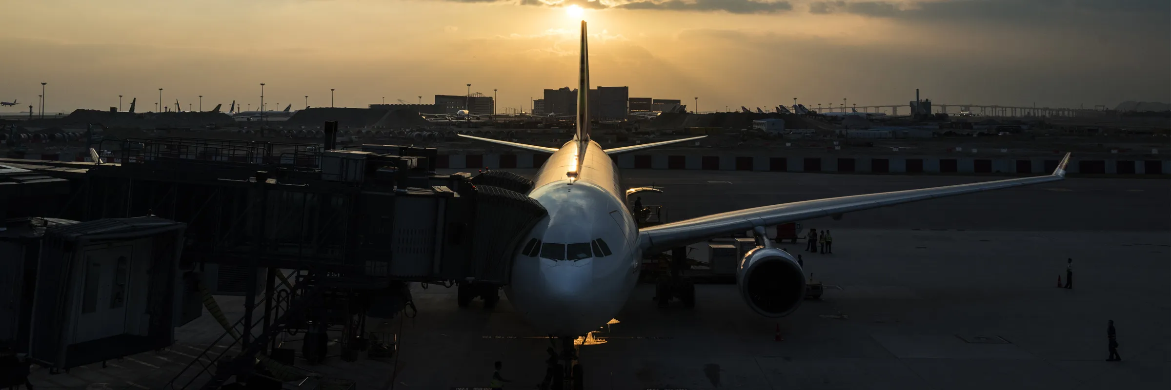 Commercial airplane parked at airport gate during sunset with workers on the tarmac.