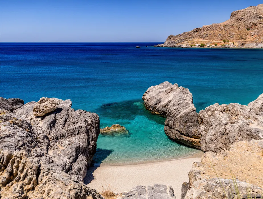 Secluded beach with clear turquoise water and rocky cliffs under a bright blue sky in Greece.