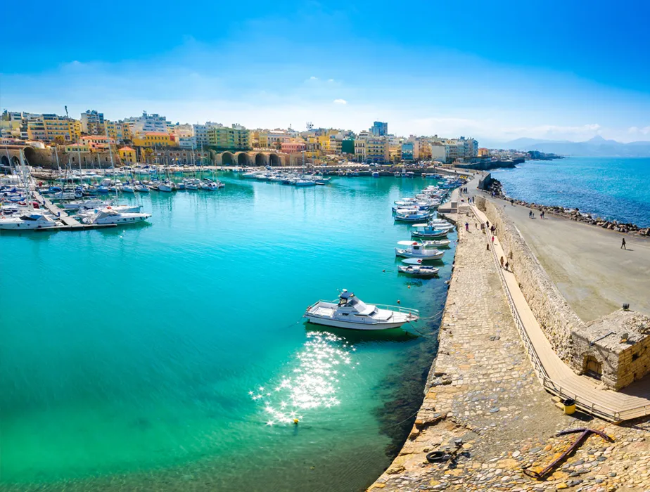 Hafen von Heraklion mit Booten vor der Küste und bunten Gebäuden im Hintergrund.