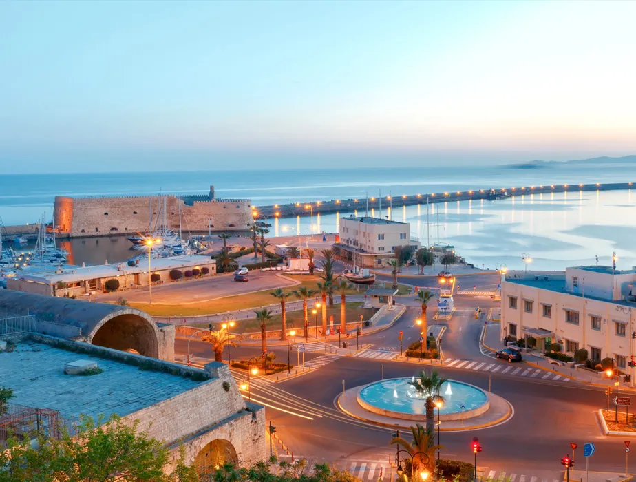 Hafen von Heraklion und venezianische Festung bei Dämmerung mit Straßenlaternen und Brunnen auf Kreta.