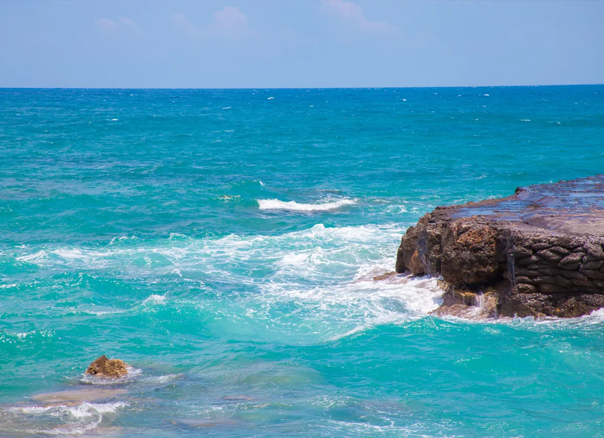 Sea waves gently breaking against rocky coastline under blue sky.