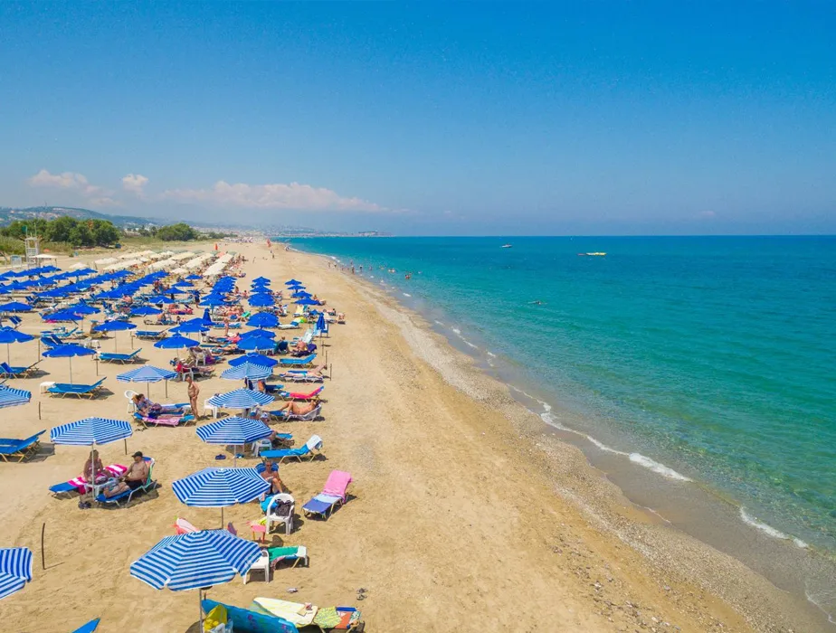 Sandy beach with blue umbrellas and sunbeds along the clear blue sea, ideal for a car rental trip.