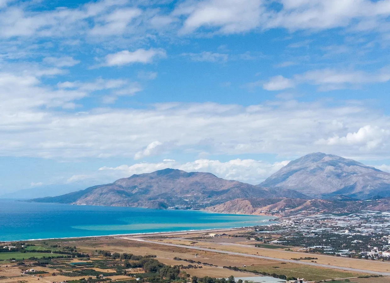 Scenic panoramic view of a coastal area with mountains, clear blue sea, and an airport runway.