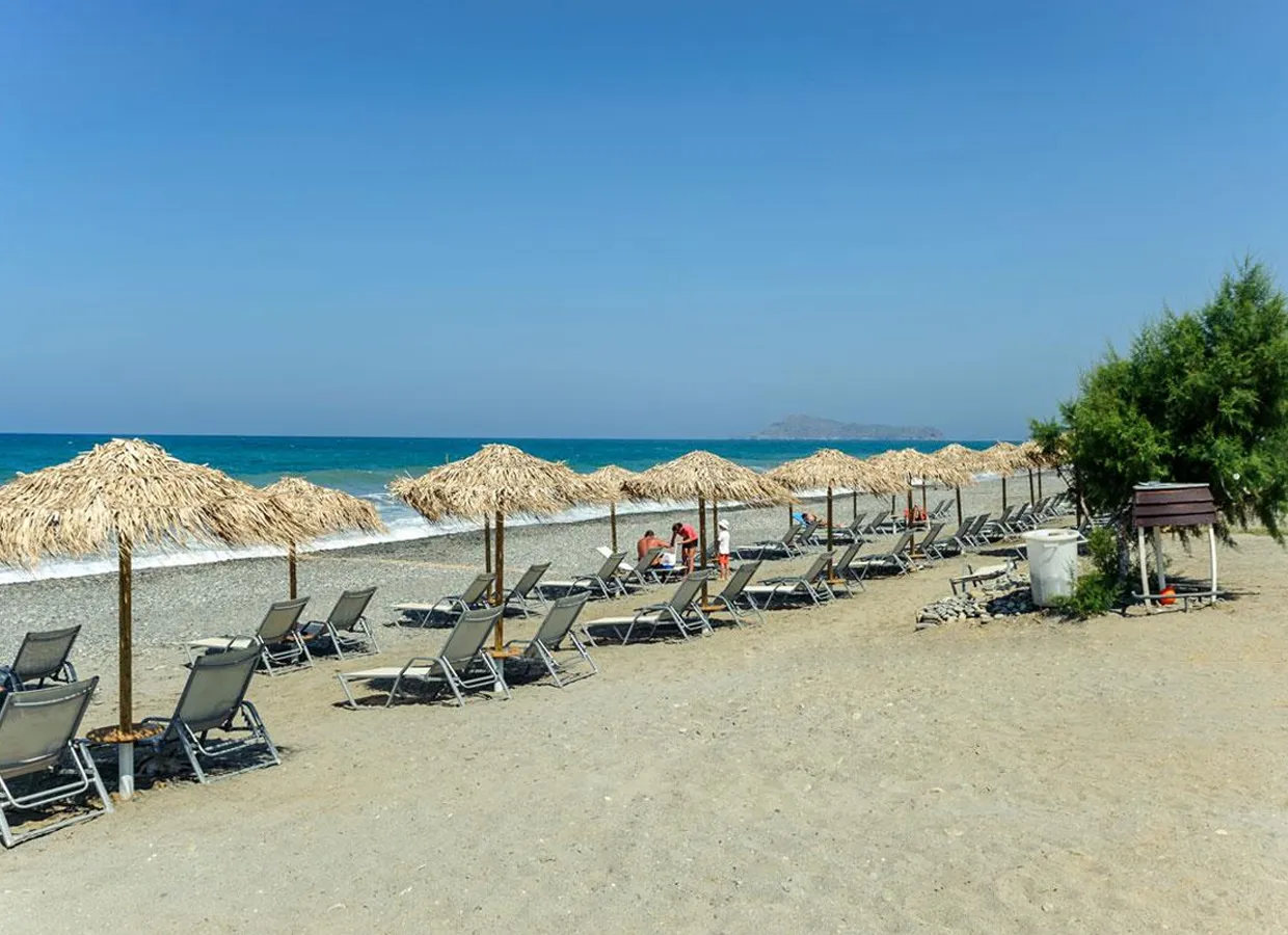 Beach with rows of sun loungers and thatched umbrellas along the sandy shore near turquoise sea water.