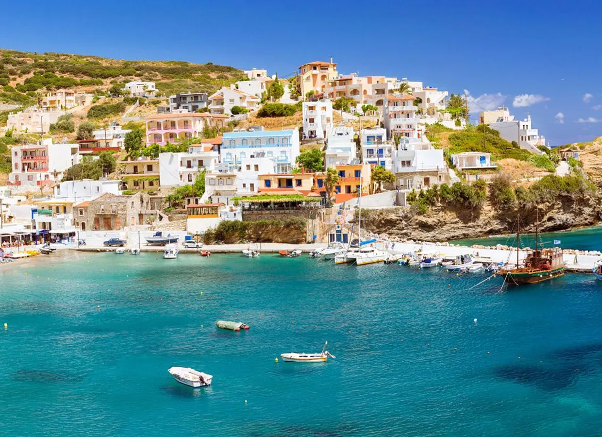 Greek island coastal village with colorful houses and boats docked in clear blue water.