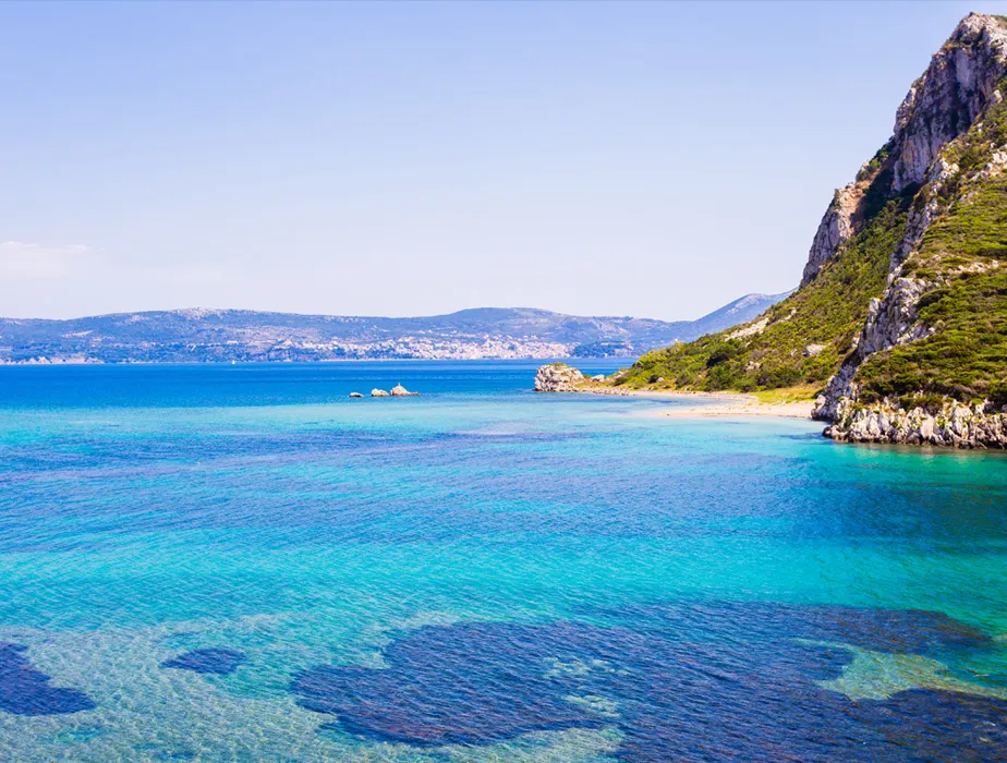 Paesaggio costiero con acqua azzurra e colline rocciose in una baia mediterranea, ideale per noleggio auto.