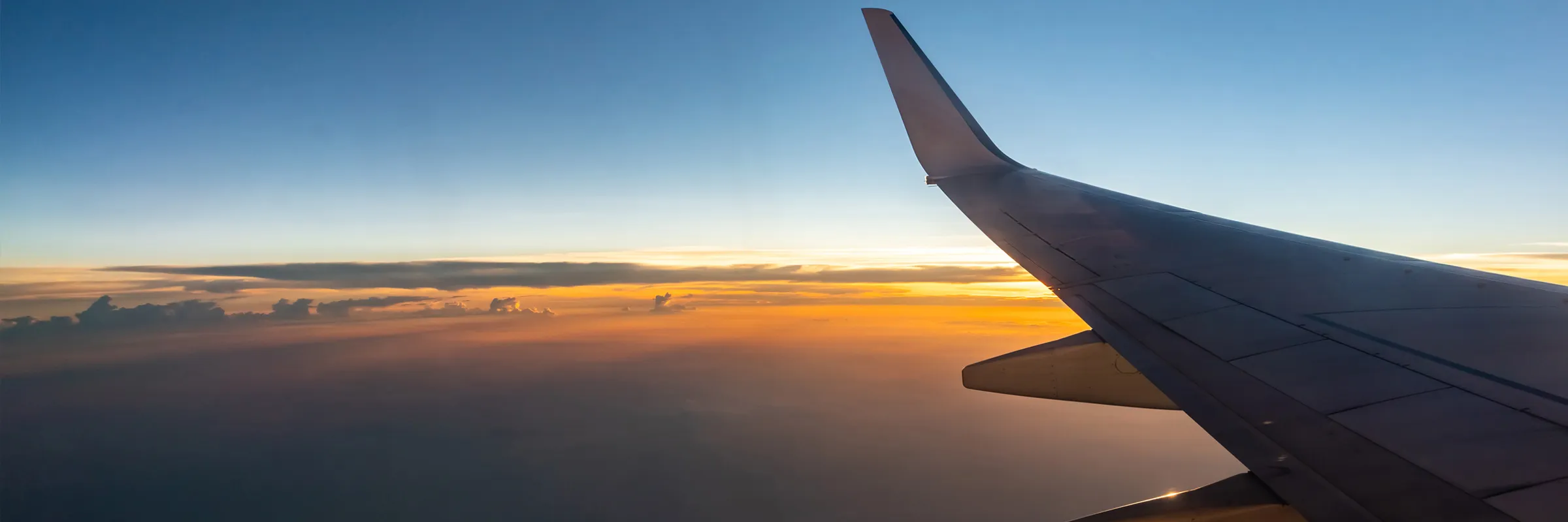 Ali dell'aereo in volo al tramonto, cielo visibile e nuvole sotto l'aeromobile.