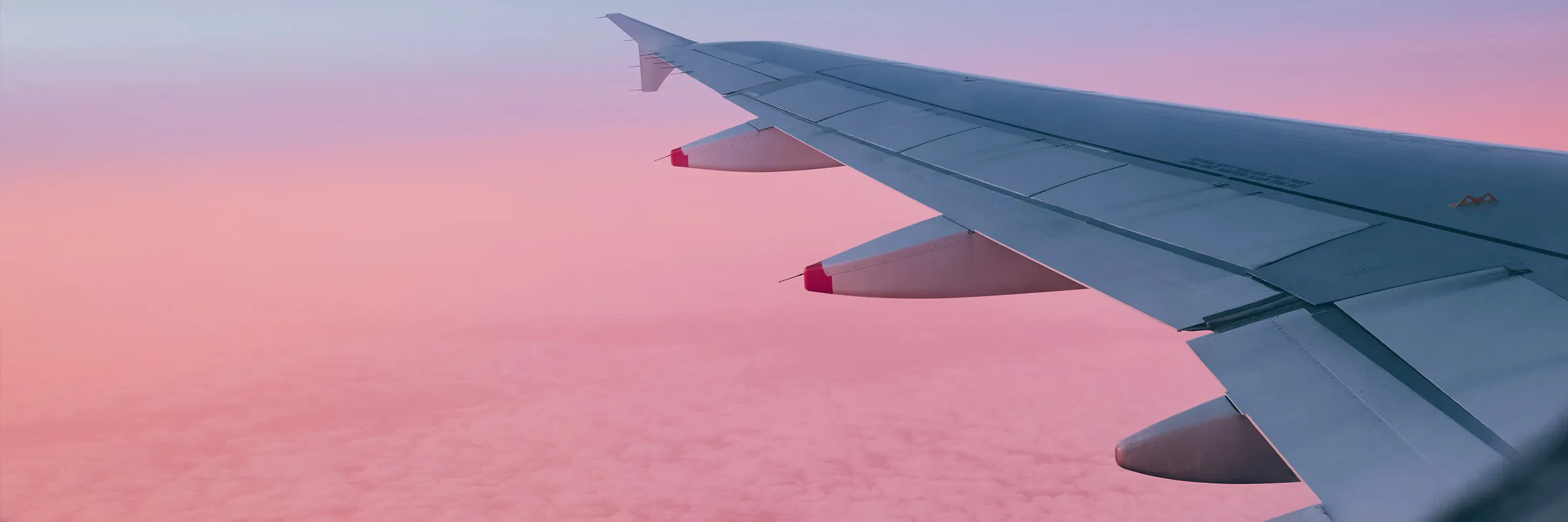 Airplane wing above clouds during a pink and purple sunset sky from a rental car user's travel.
