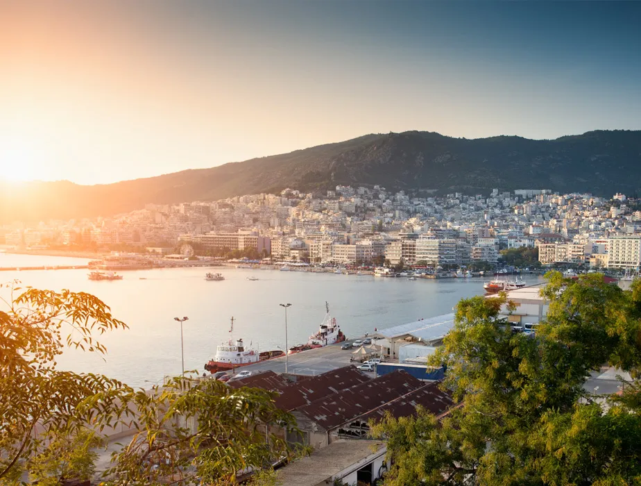 Kavala port and cityscape at sunset with calm waters and hillside buildings.