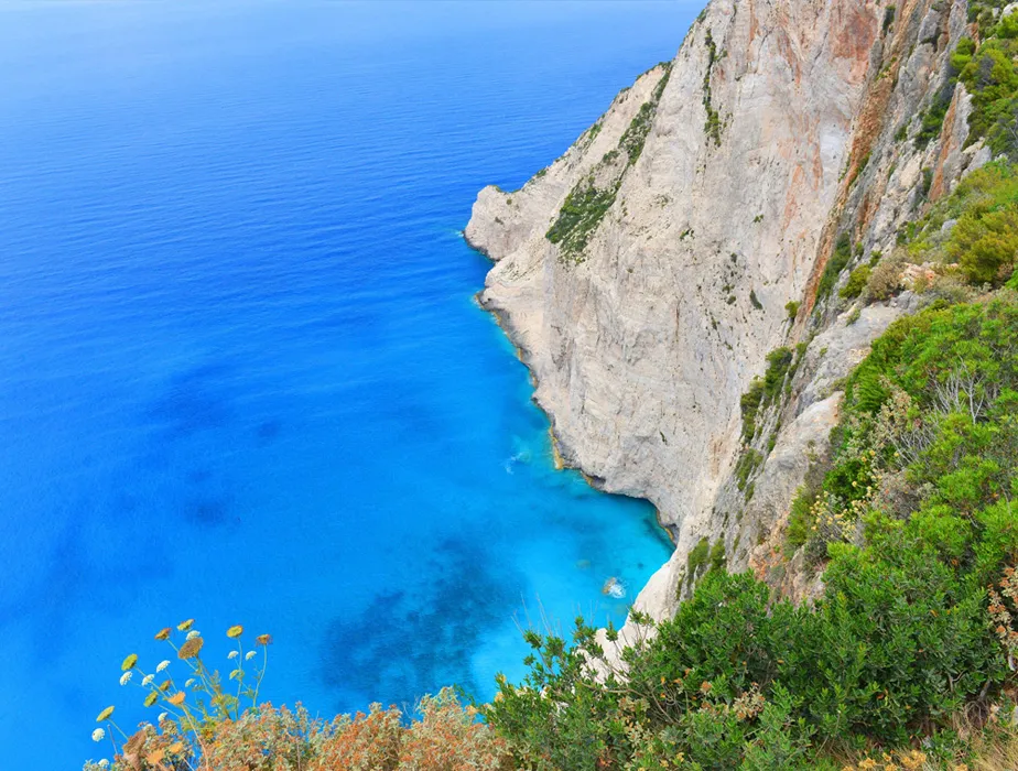 Costa di Zante con scogliere che si affacciano sul mare blu e vegetazione verde vicino al bordo.
