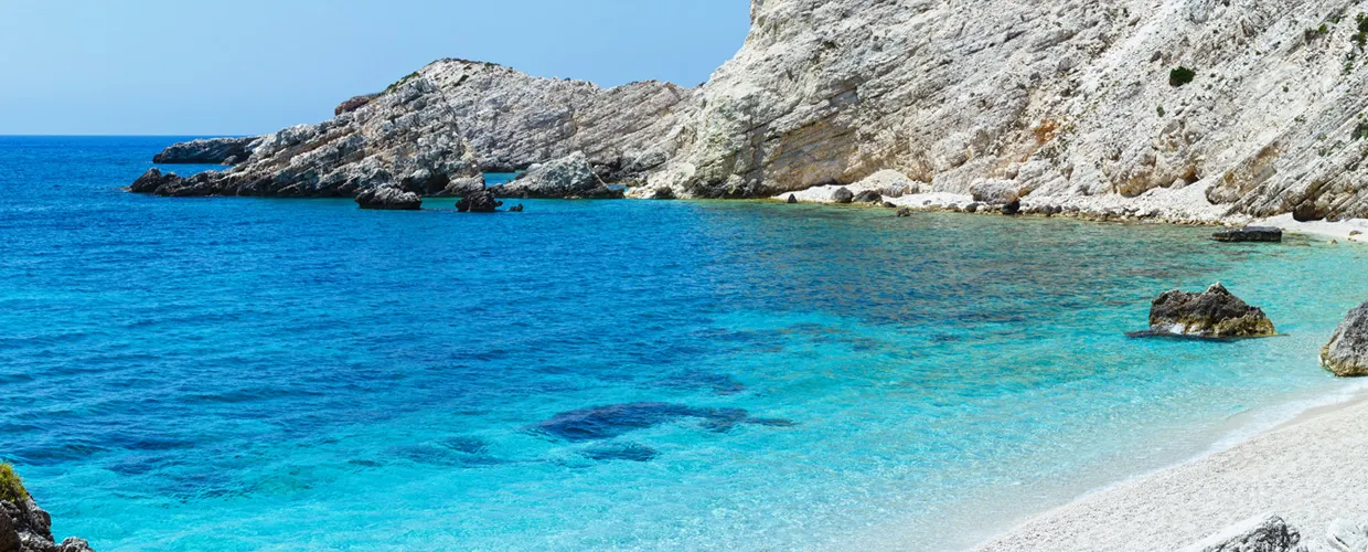 Acqua turchese limpida lungo una costa rocciosa con piccola spiaggia, perfetta per viaggi in auto a noleggio.