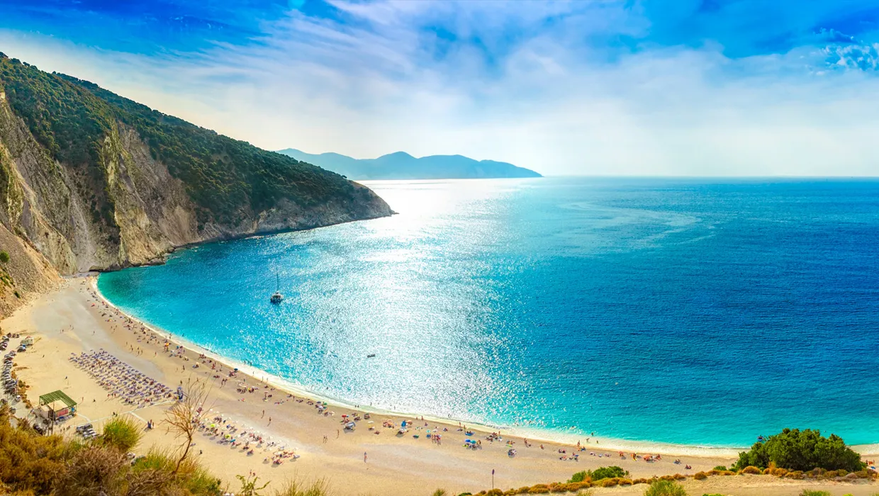La spiaggia di Myrtos a Cefalonia con mare blu e scogliere, luogo ideale per noleggio auto.