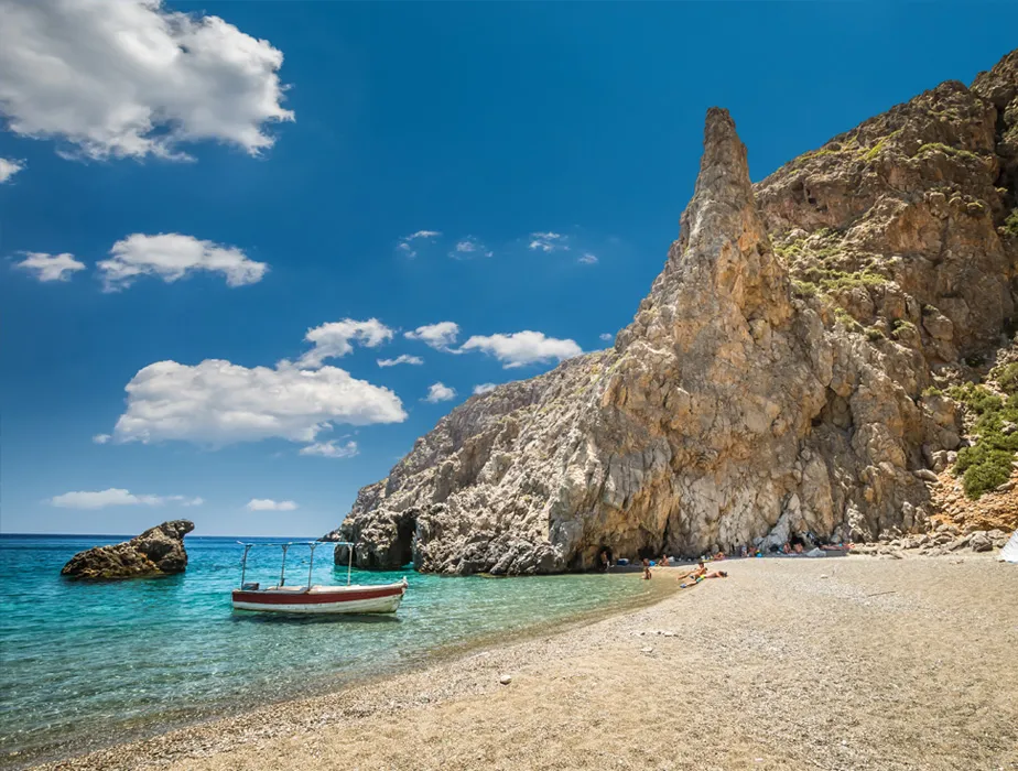 Plage isolée avec un petit bateau sur une eau turquoise claire et des falaises rocheuses au soleil.