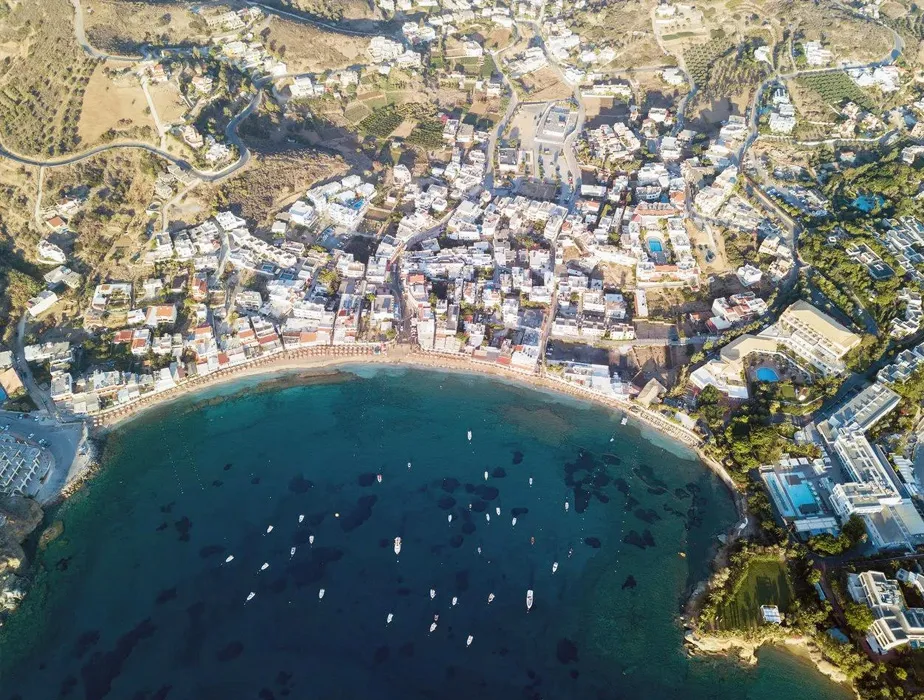 Baie d'Agios Nikolaos avec plage, bâtiments et bateaux en Crète pour options de location de voiture.