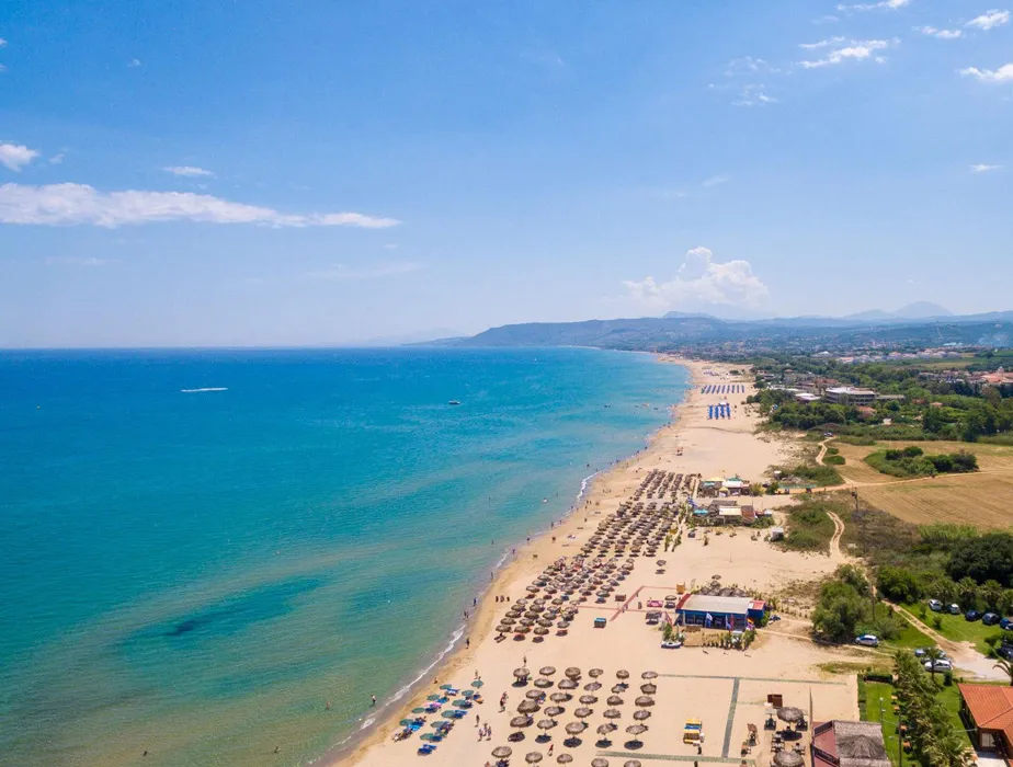 Spiaggia costiera con ombrelloni e mare azzurro limpido che si estende lungo la riva in una giornata di sole.