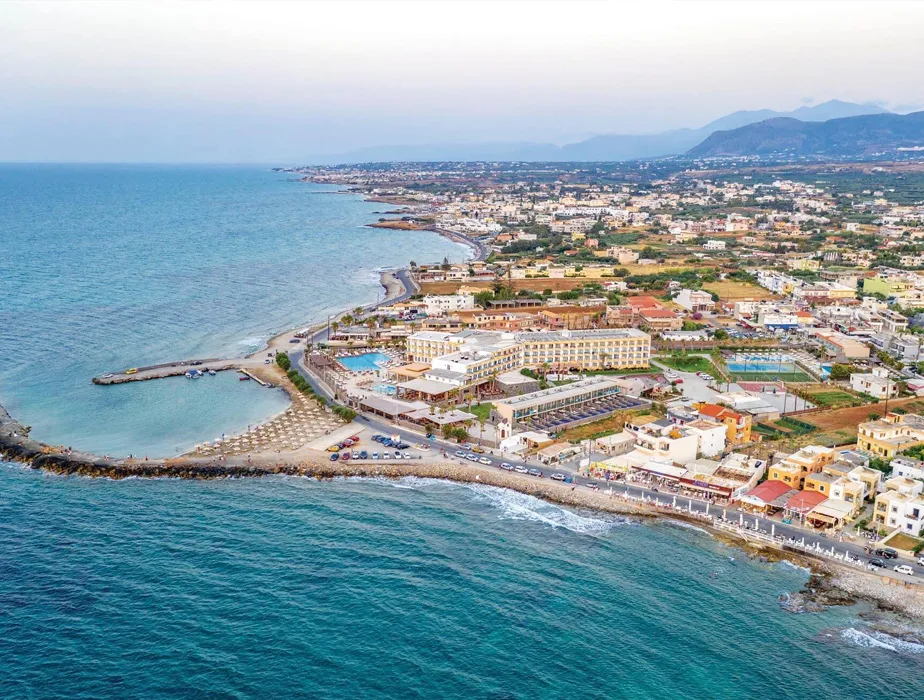 Vista aerea della città costiera con spiagge, hotel e montagne in lontananza.