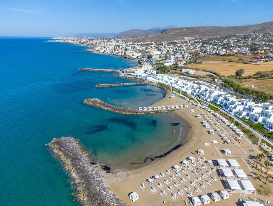 Veduta aerea di una spiaggia sabbiosa con ombrelloni e città costiera a Creta per noleggio auto.