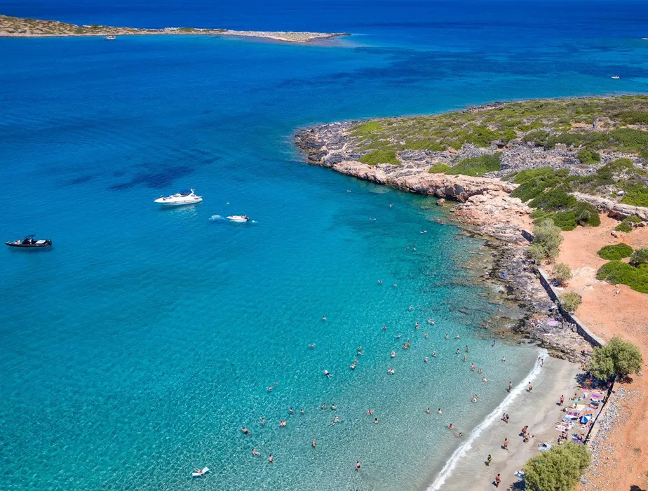 Mare limpida con nuotatori e barche vicino a una costa rocciosa e una spiaggia.