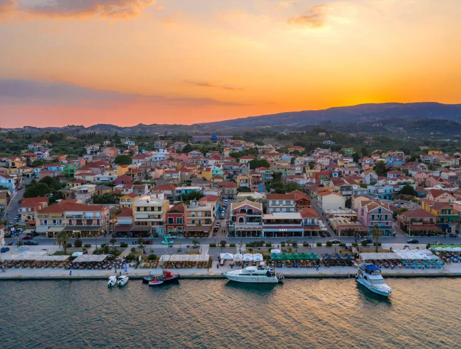 Sunset over Gaios town with waterfront, boats, and colorful buildings in Paxos, Greece for car rental exploration.