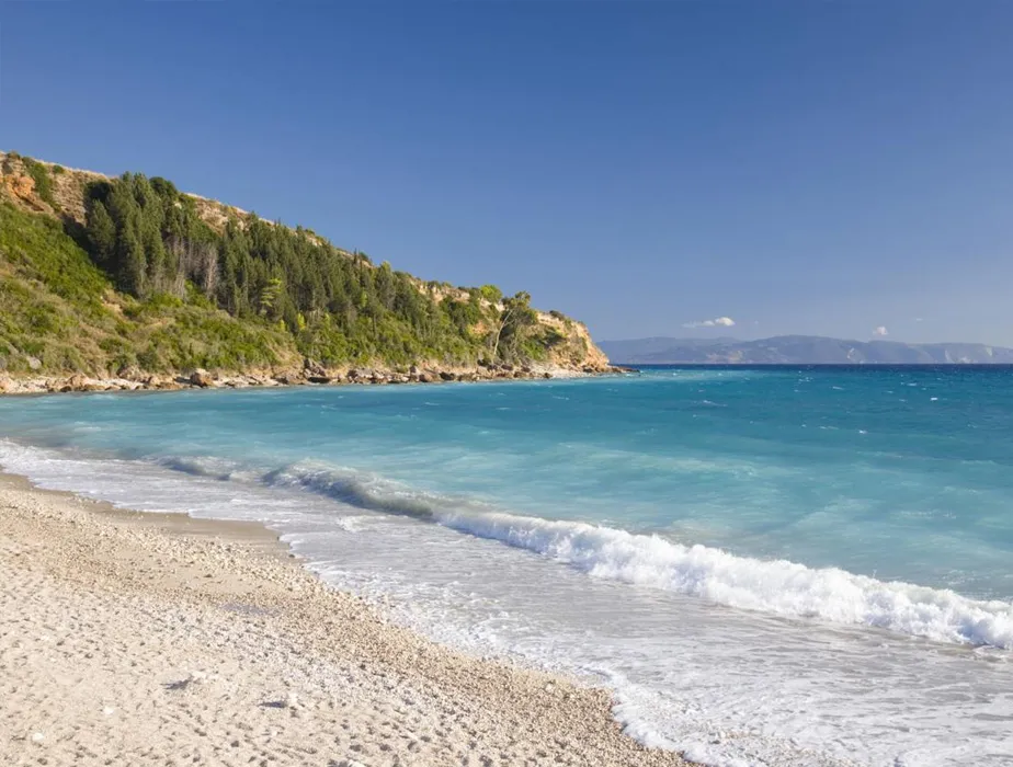 Coastal beach with turquoise water and green cliffs under a clear blue sky, ideal for a coastal drive.