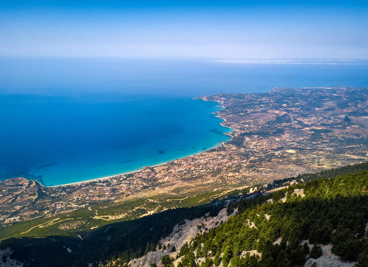 Coastal landscape view with clear blue water and forested hills ideal for a scenic car rental drive.