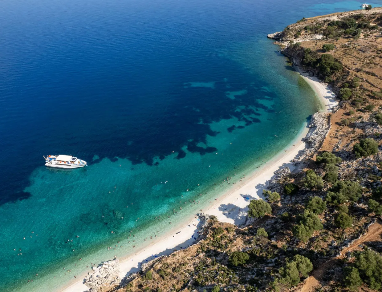 Coastal beach with turquoise water and a white boat near the shore, perfect for summer car rental trips.