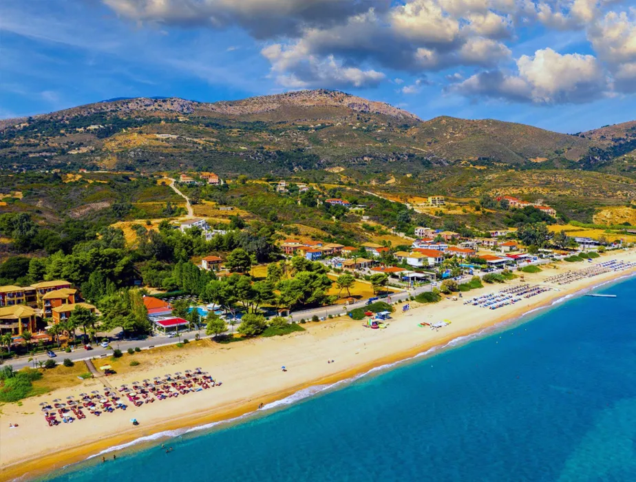 Beachfront with umbrellas and sunbeds along the coast and hills with scattered houses behind, peaceful landscape.