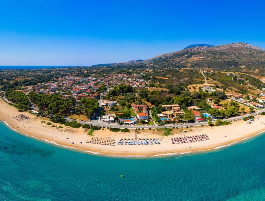 Aerial view of Kokkari beach in Samos with clear blue water and sun umbrellas along the shore.