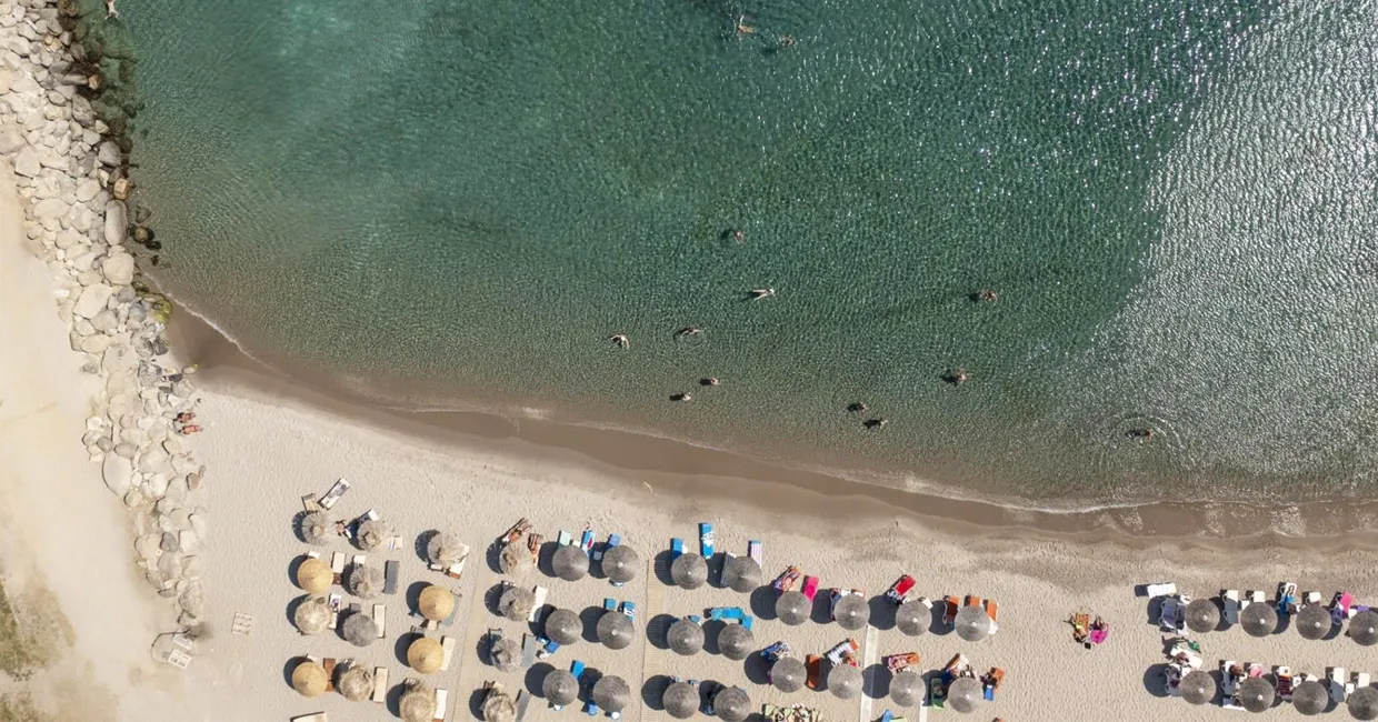 Aerial view of a beach with sunbeds, umbrellas, and people swimming in clear water.