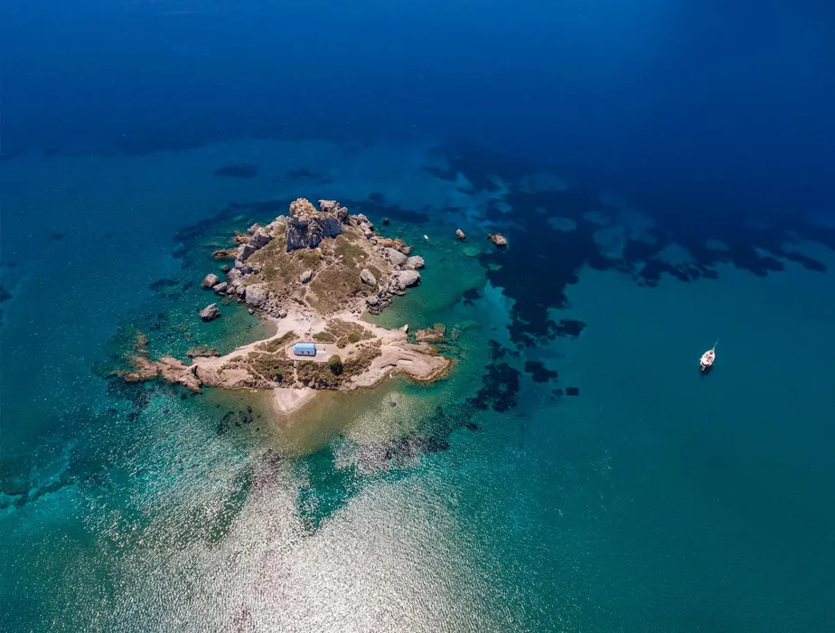 Small rocky island with clear turquoise water and a solitary boat nearby in the sea.