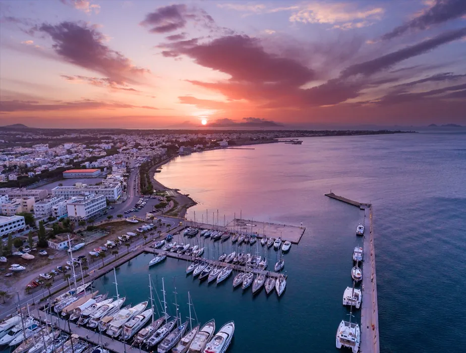 Naxos port at sunset with boats docked and calm sea reflecting colorful sky.