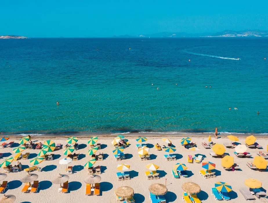 Greek island beach with umbrellas and sunbeds by the clear blue sea, ideal for summer vacations.