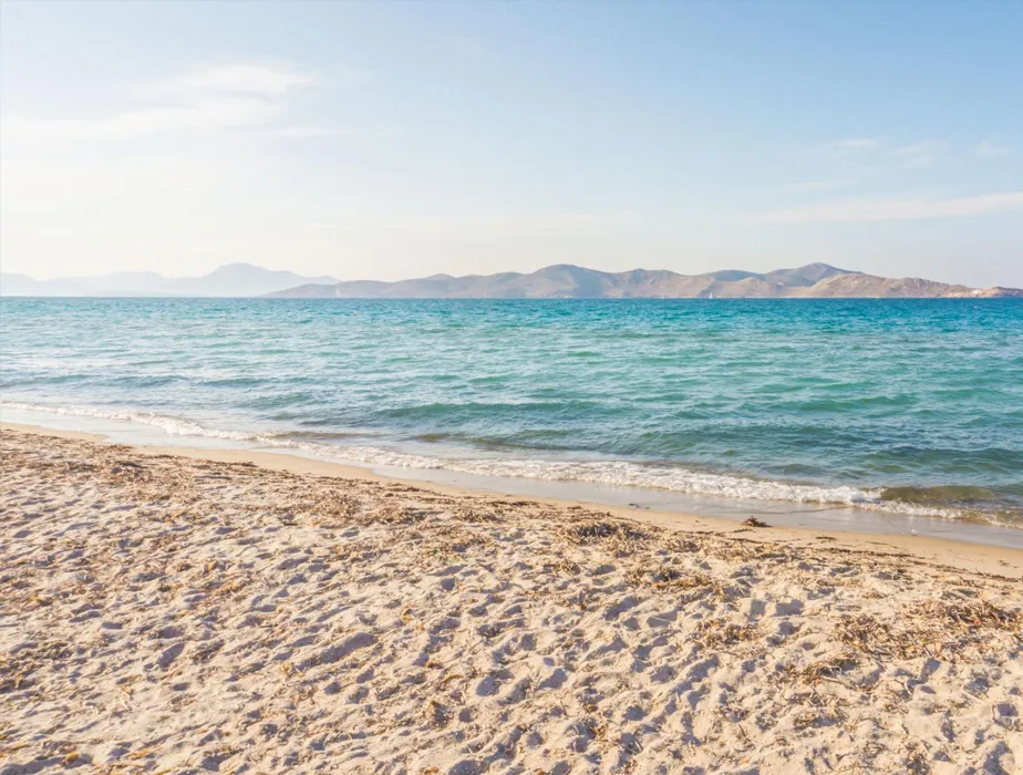 Sandy beach with gentle waves and distant hills under a clear sky, perfect for a coastal rental getaway.