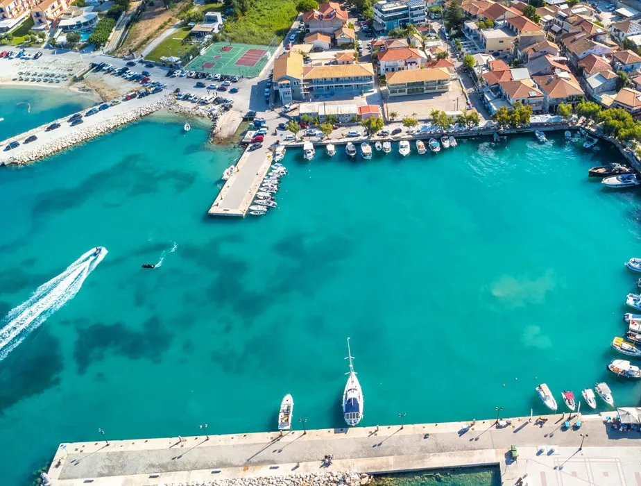 Coastal town harbor with boats docked along turquoise water and waterfront buildings.